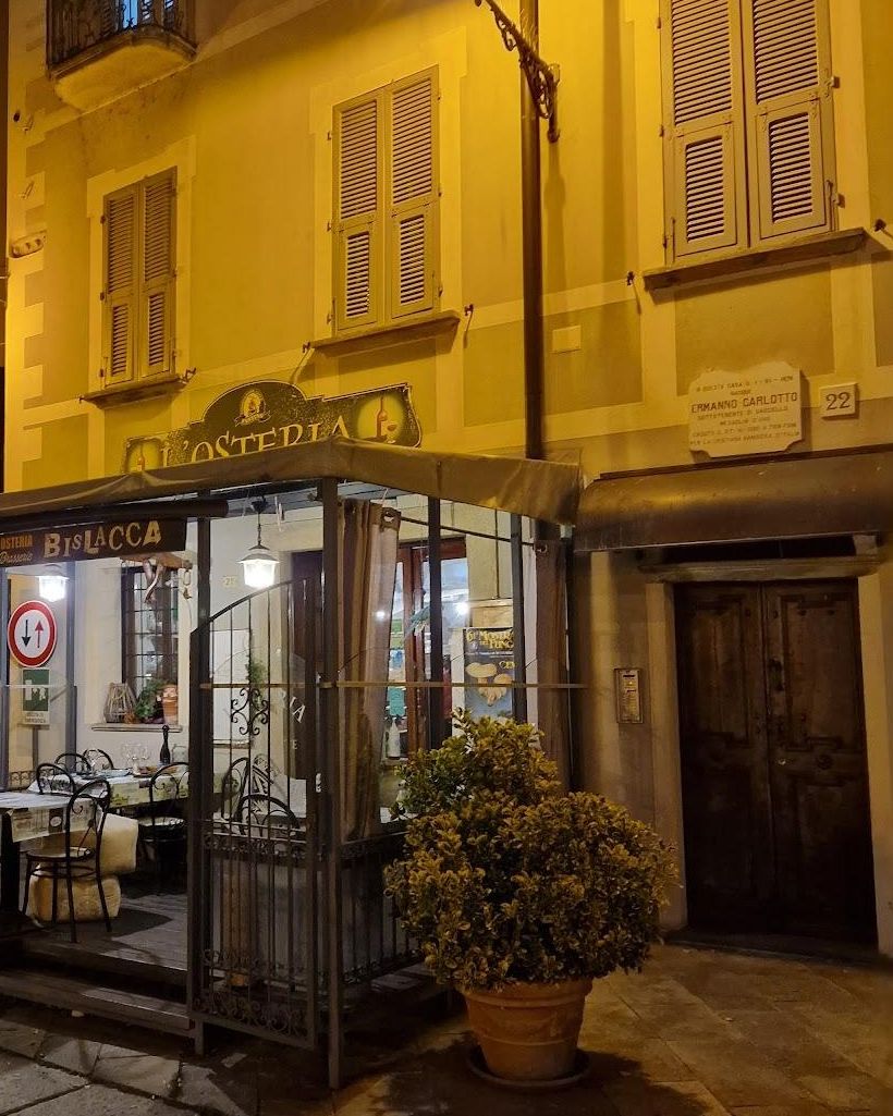 Il dehors dell'Osteria Bislacca in piazza, di sera, sotto l'insegna